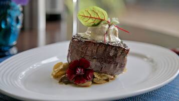 Un plato con un trozo de carne, una flor roja y una hoja verde como adorno.