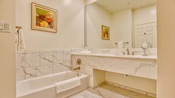 A bathroom with a bathtub, a large mirror, and a marble-tiled floor.