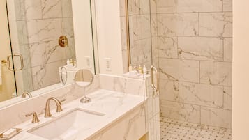 A modern bathroom with a marble vanity, a large mirror, a glass-enclosed shower, and a tiled floor.