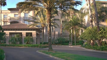 A multi-story hotel with a central courtyard, palm trees, and a well-maintained lawn.