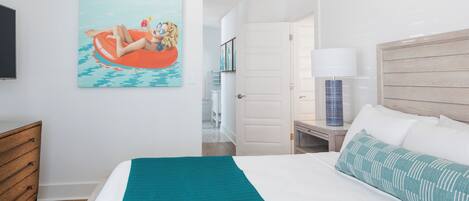 A bedroom with a bed, a nightstand, a lamp, a wooden dresser, and a painting on the wall.