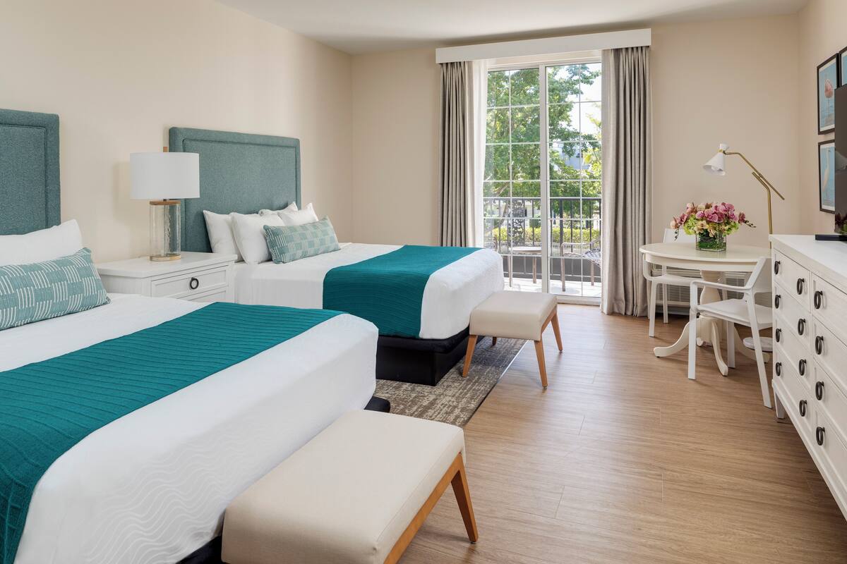 Habitación de hotel con dos camas, una mesita con lámpara, una silla y un aparador.