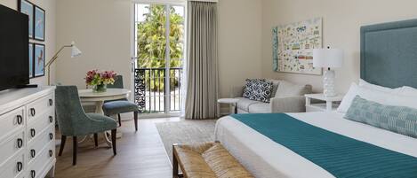 A hotel room with a large bed, a desk with a chair, a bench, a TV, and a balcony with curtains.