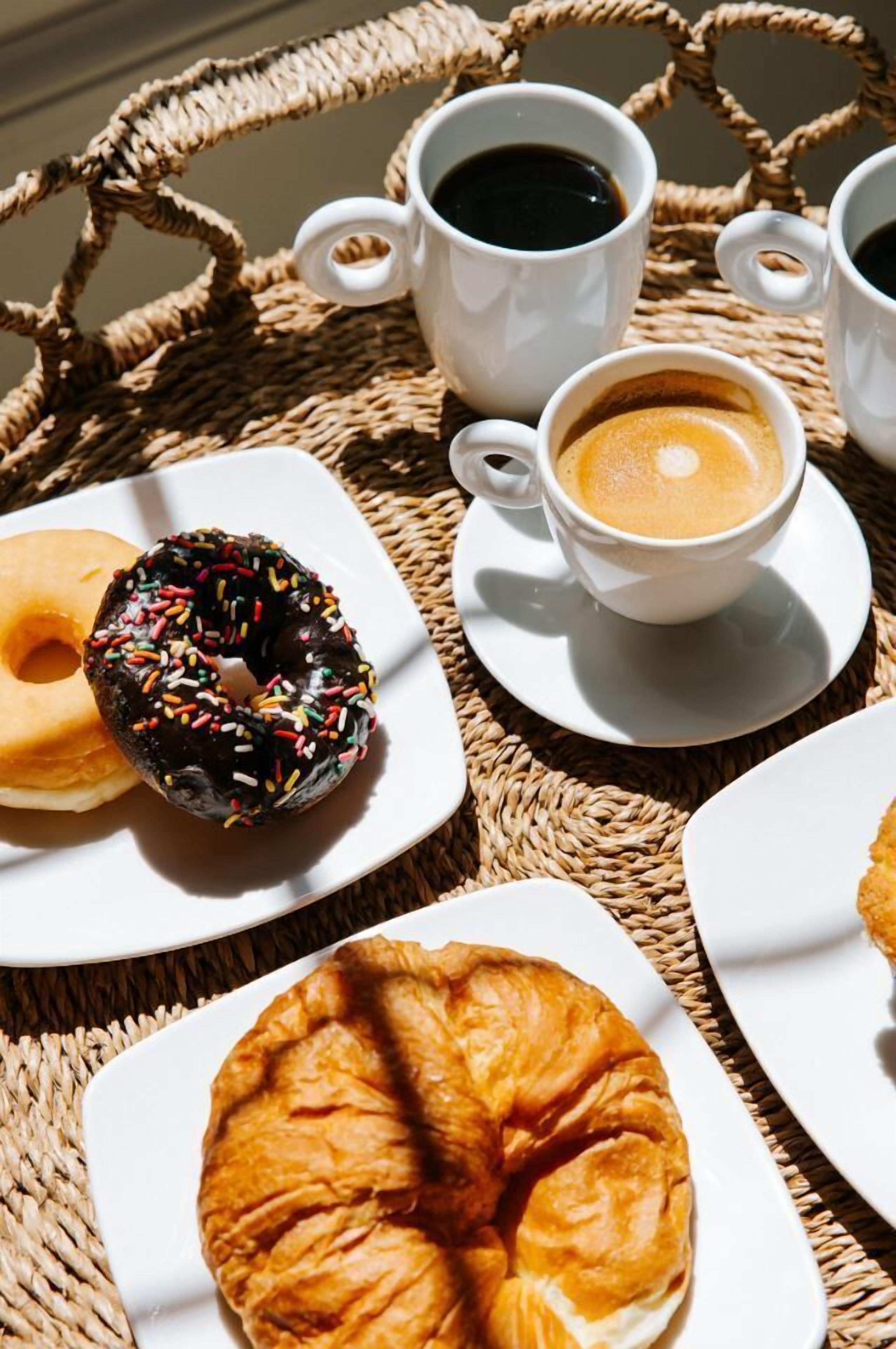 A wicker table with a croissant, a donut, and two cups of coffee.