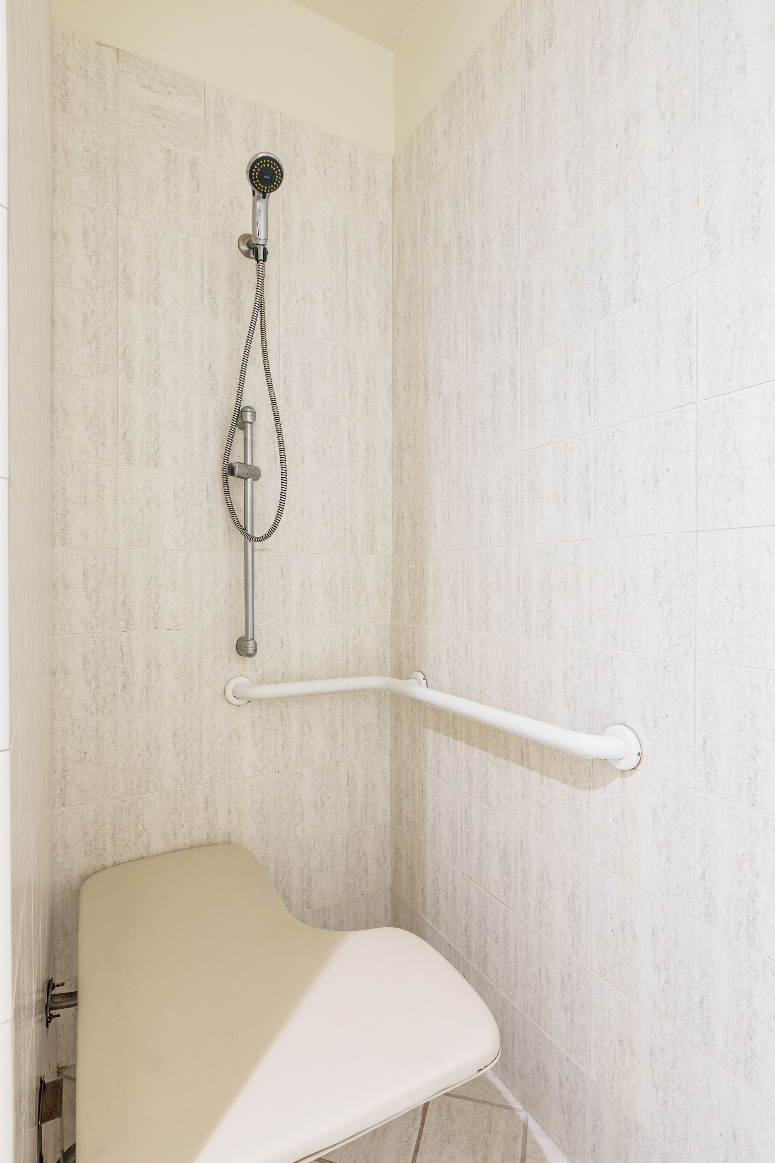 A shower area with a grab bar, a handheld showerhead, and a white seat.