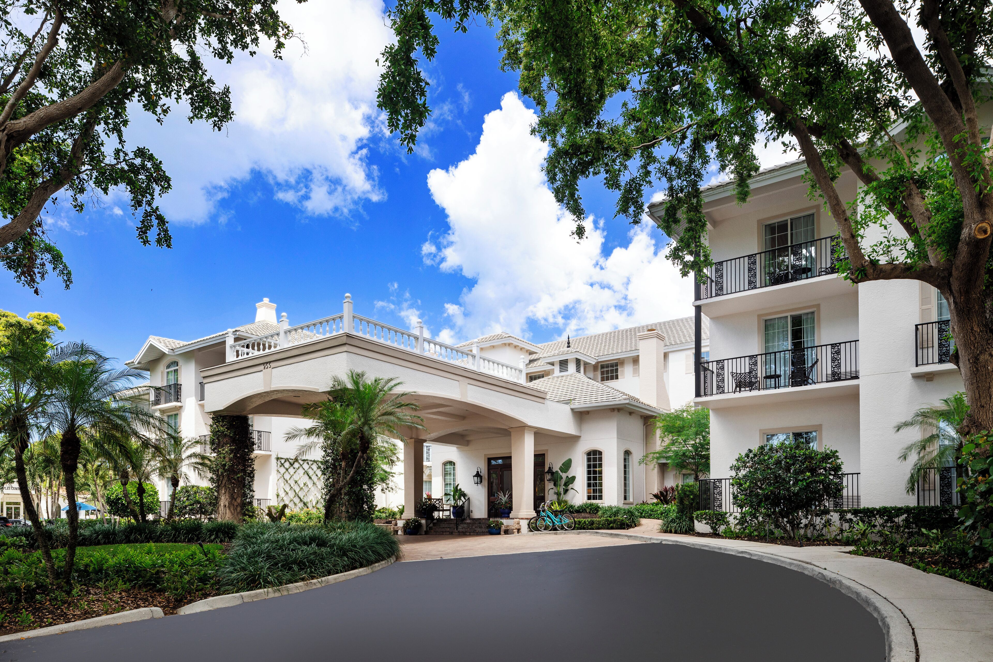 Un grand bâtiment blanc, doté d’une entrée imposante, de nombreux balcons et d’un aménagement paysager luxuriant.