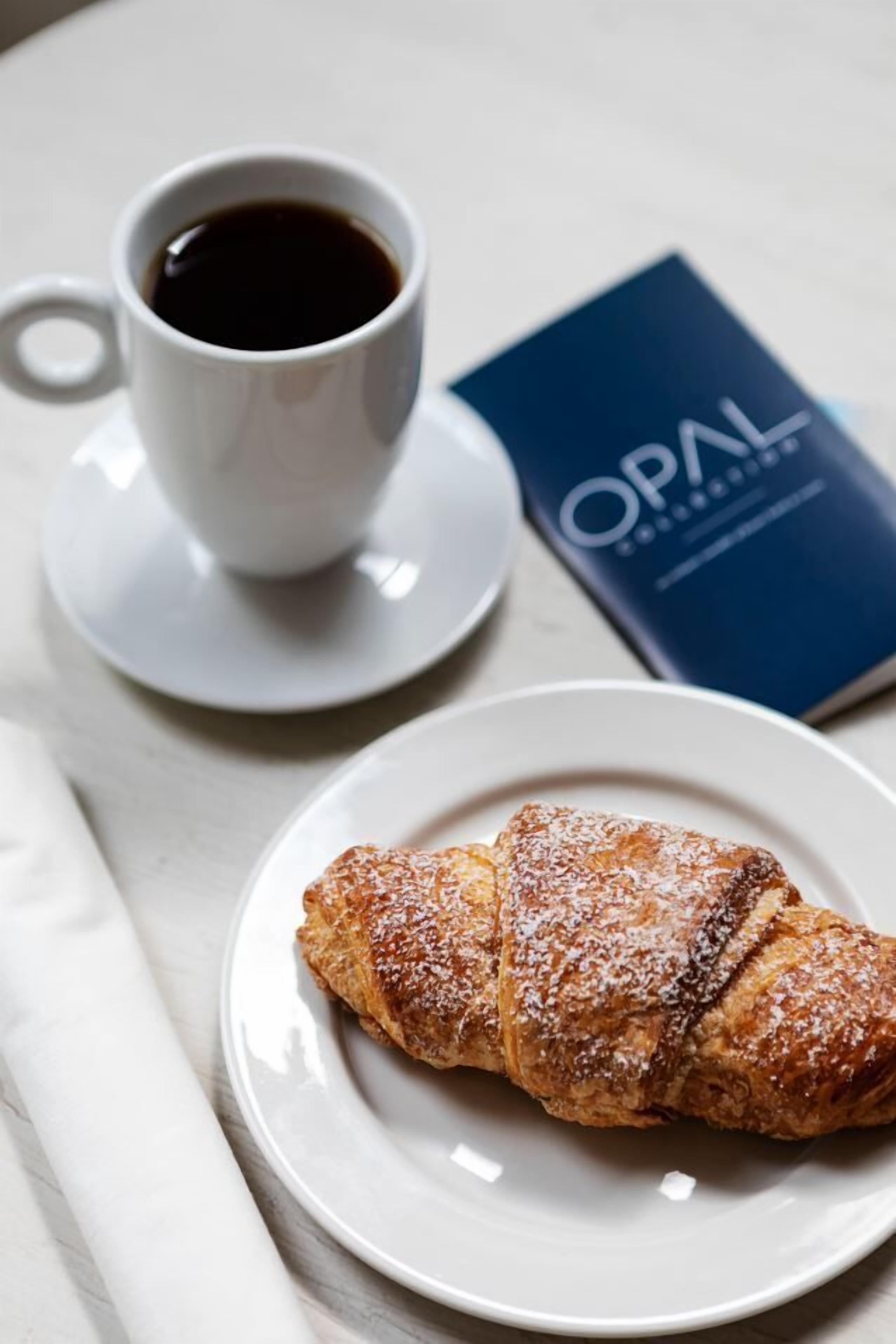 Un croissant sur une assiette, une tasse de café et un livre intitulé « OPAL » sur une table.