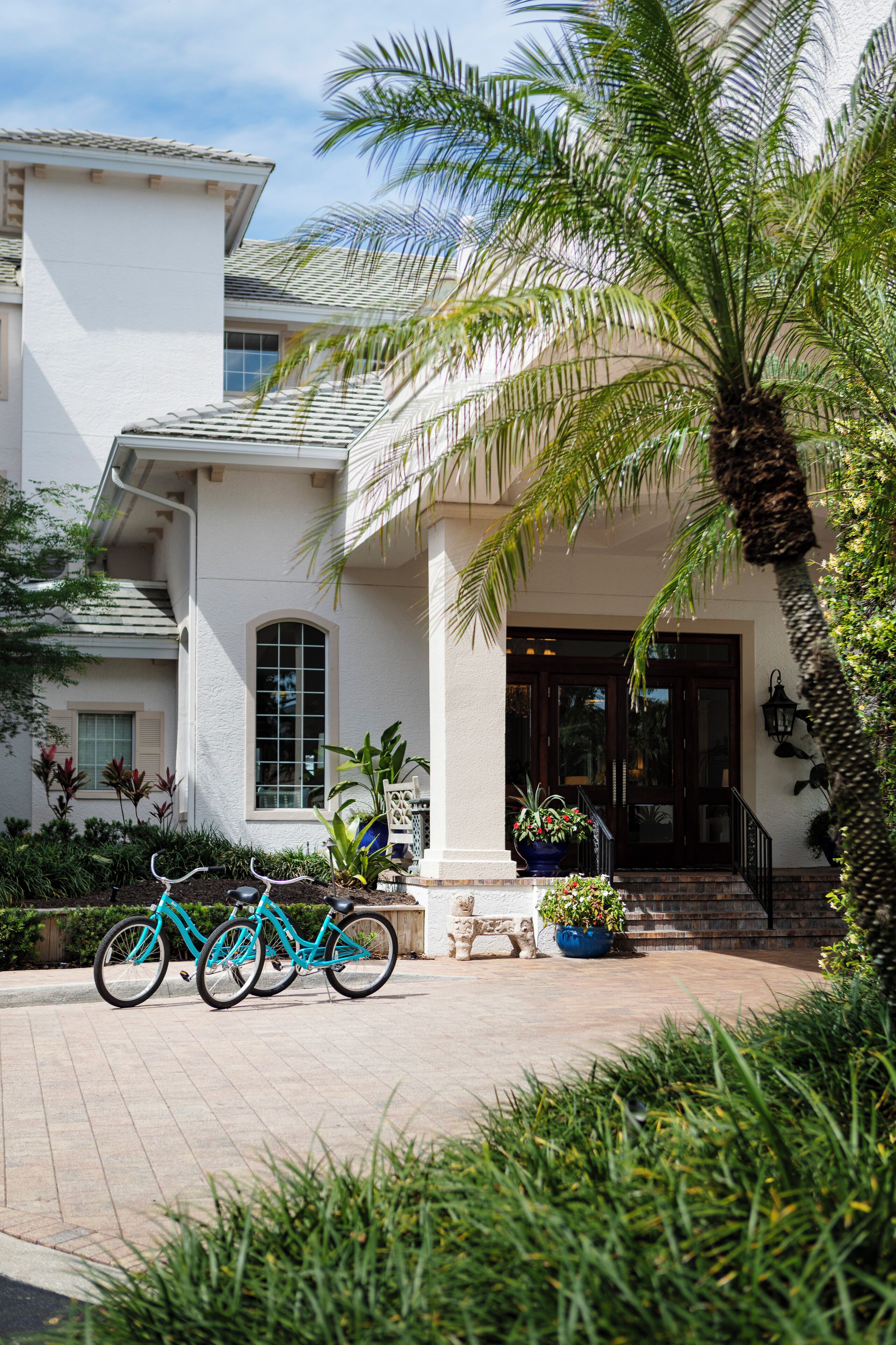 A white building with a tiled roof, a front entrance with a staircase, and two bicycles parked in front.