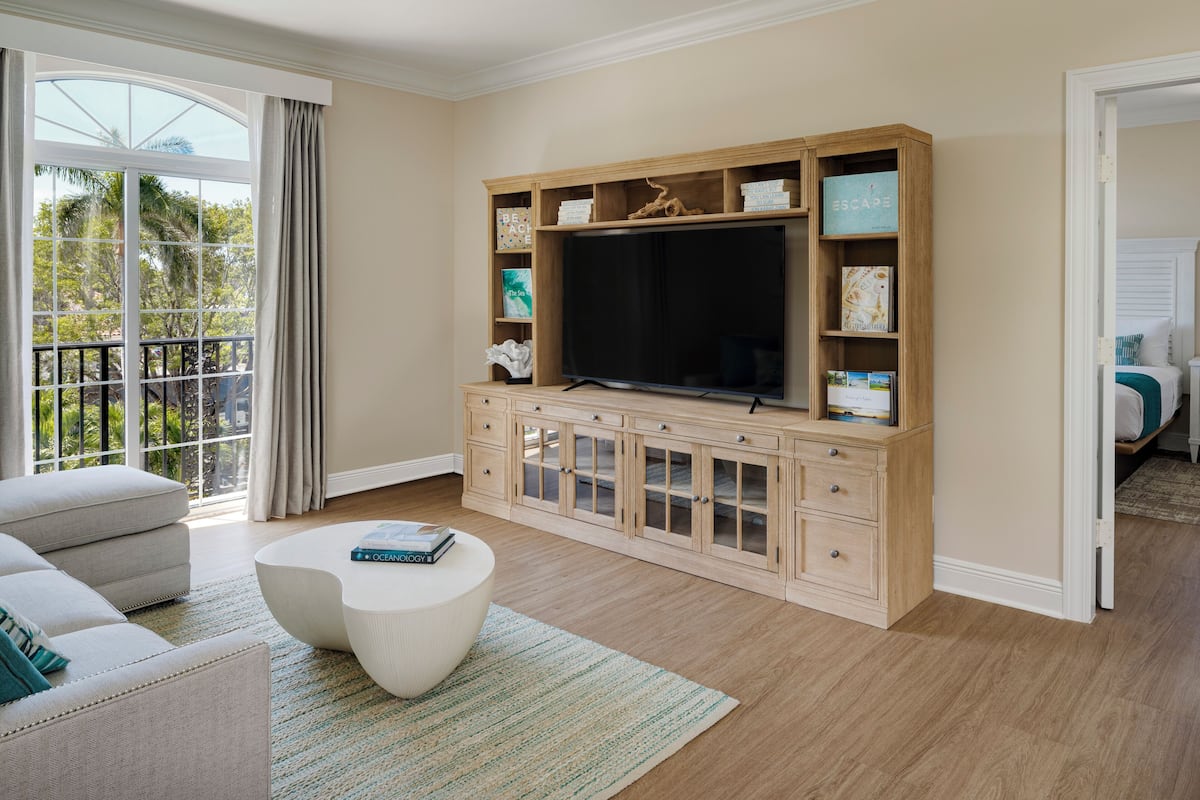 Una sala de estar con un televisor de pantalla plana grande, un sofá blanco, una mesa de centro redonda y un mueble de madera con estantes.