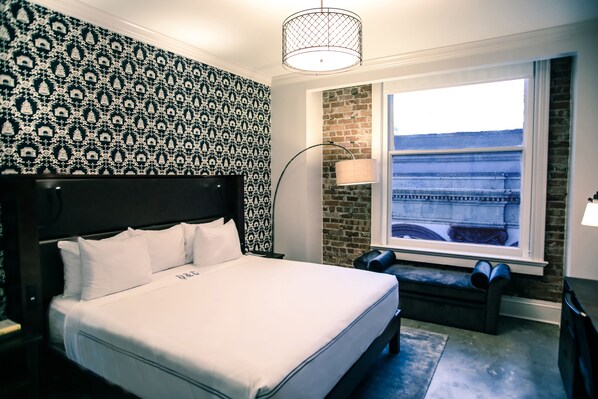 Una habitación de hotel con una cama grande, un muro decorado con ladrillos, una ventana con vistas y un papel tapiz estampado.
