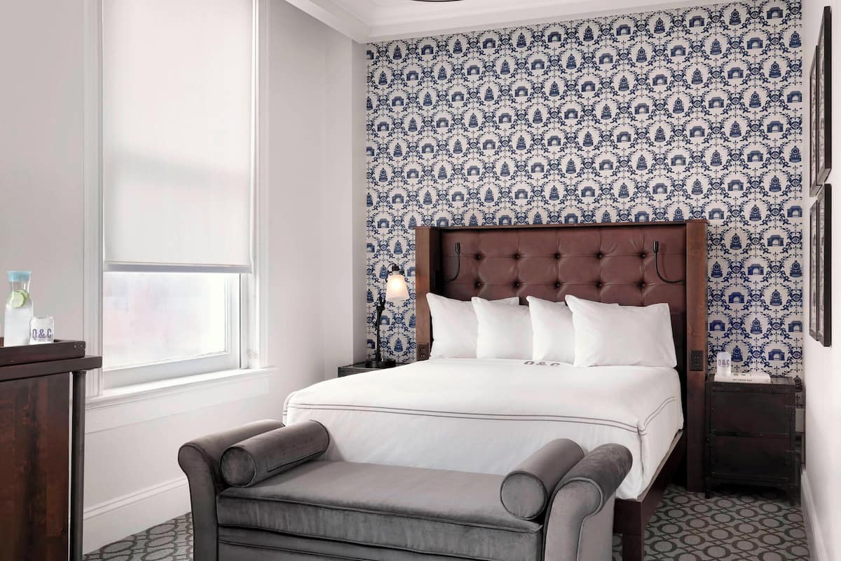 Une chambre bien rangée, avec un grand lit, une table de chevet, une lampe et une chaise.