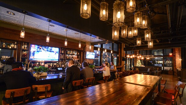 Un bar avec des tables en bois et des luminaires suspendus.