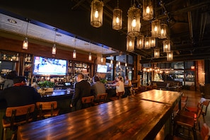 Un bar con mesas de madera y lámparas colgantes.