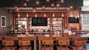 Un espace bar avec des meubles en bois, des luminaires suspendus et une grande enseigne indiquant « HÔTEL / BAR Q&C ».