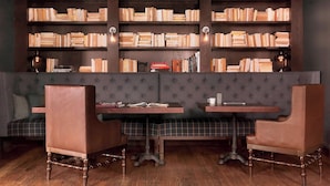 Une bibliothèque avec des étagères, deux fauteuils en cuir, une table et un banc.