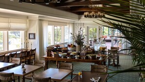 A dining area with wooden tables and chairs, a buffet table with various food items, and large windows allowing natural light.