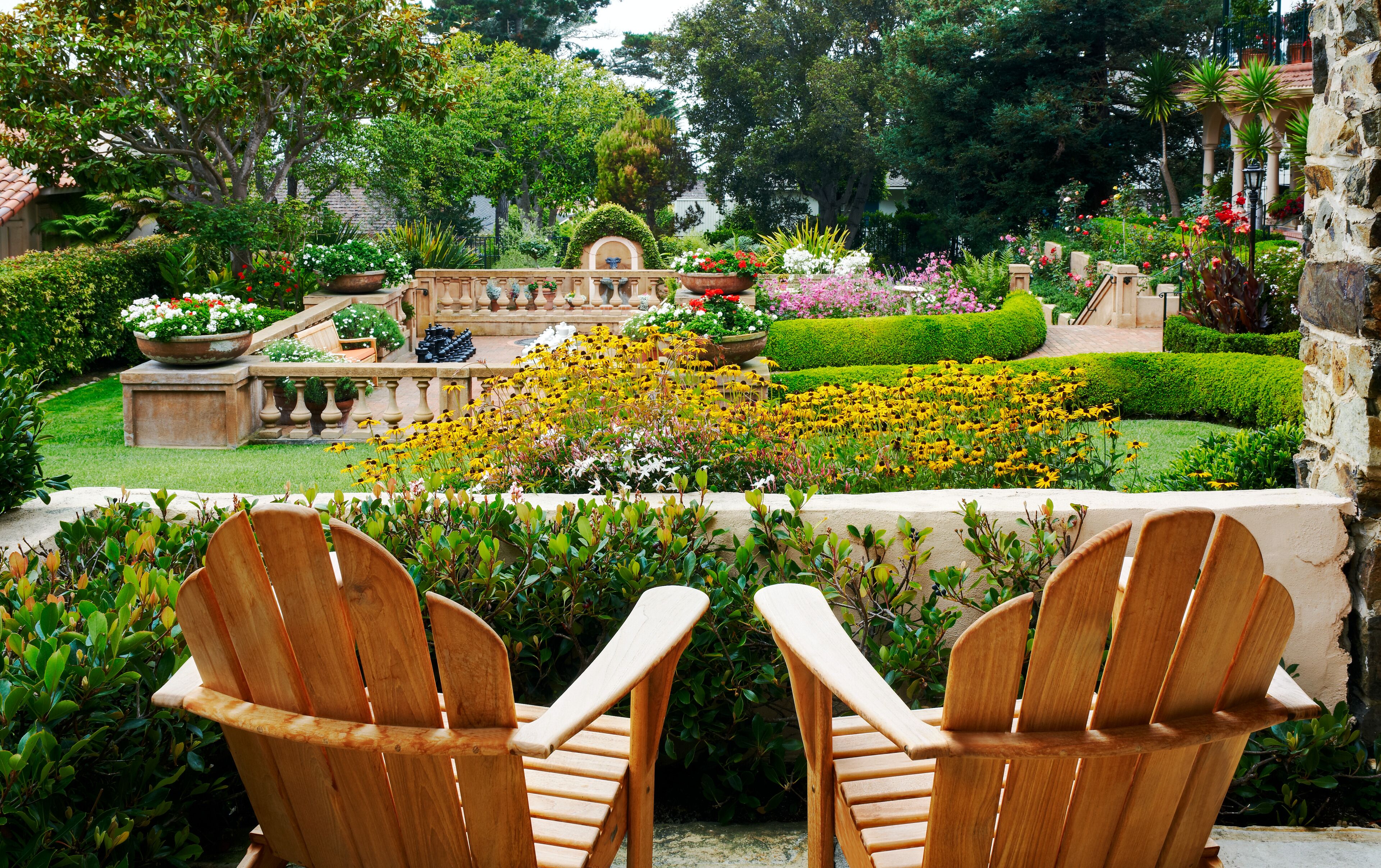 Duas cadeiras de madeira Adirondack viradas para um jardim com diversas plantas e flores.