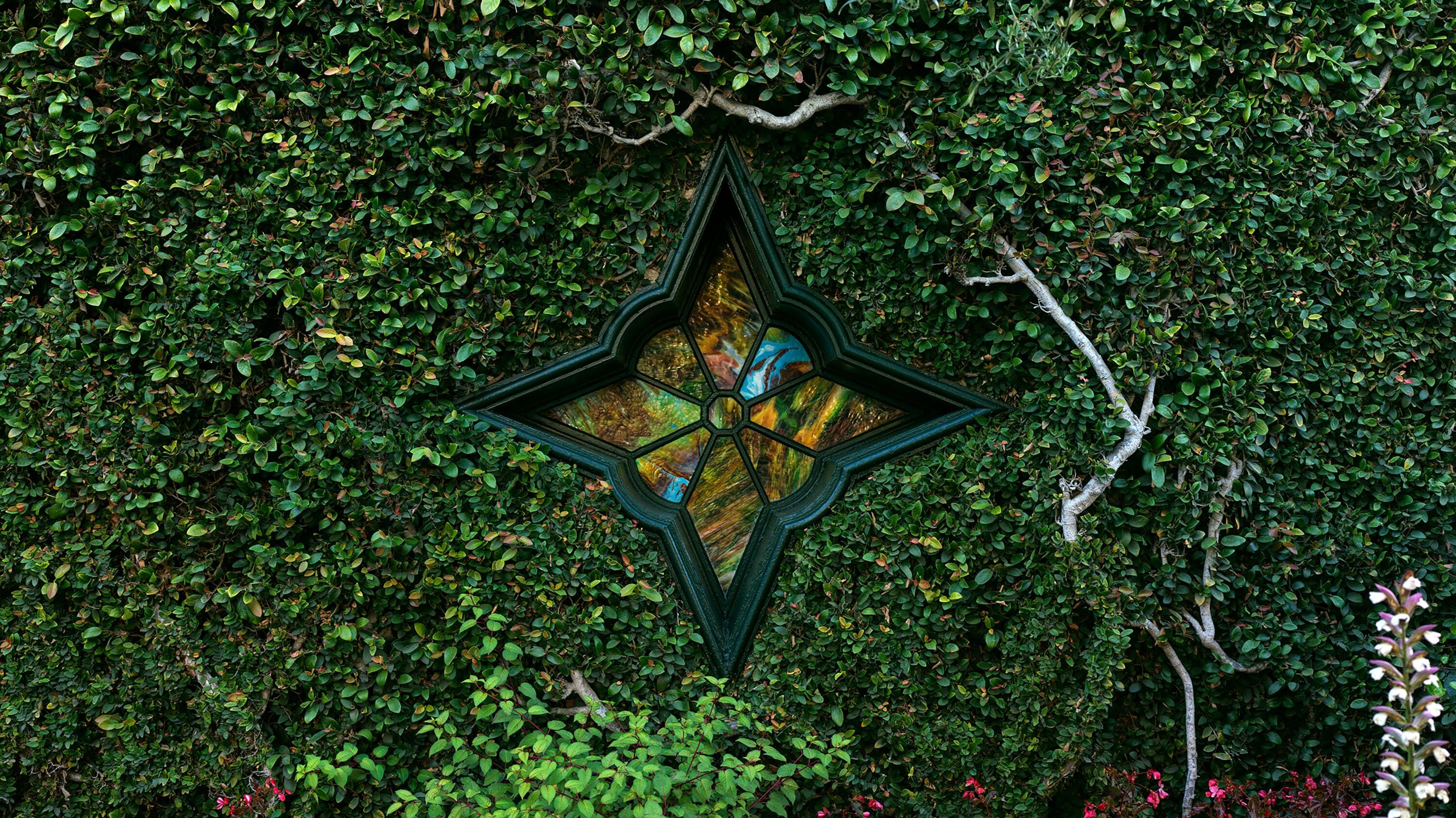 A geometric metal structure with a star-like design, surrounded by dense green foliage.
