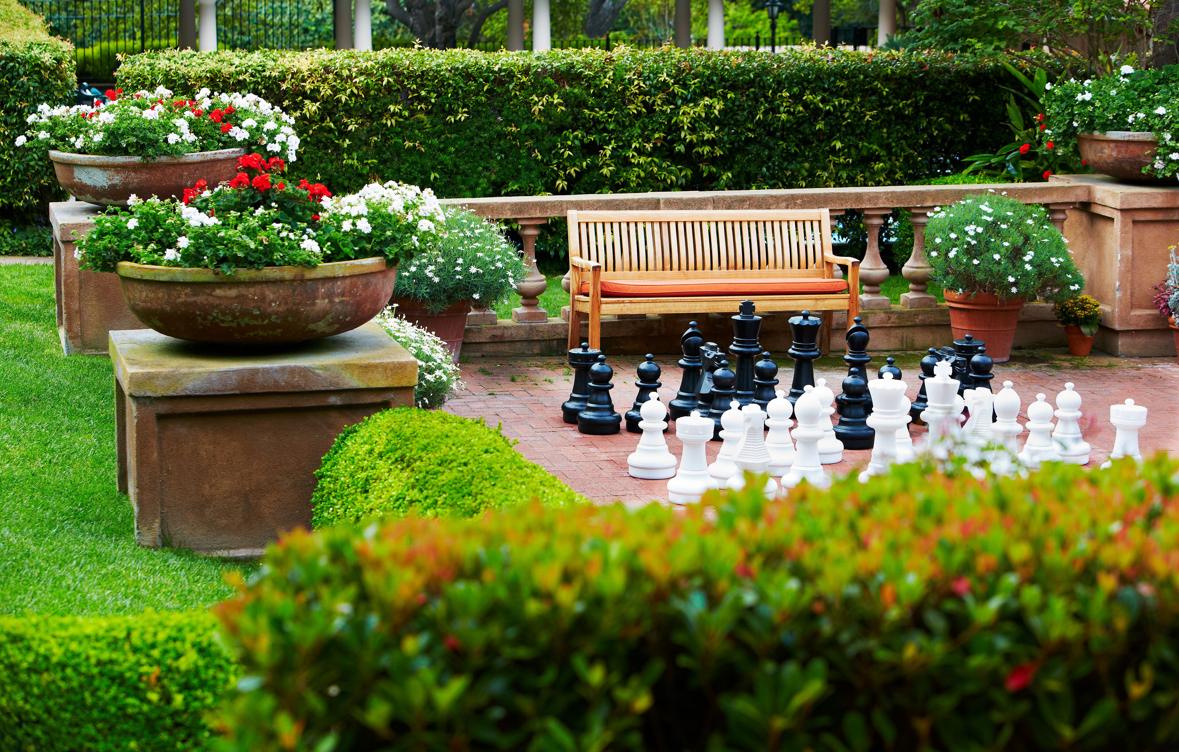 A chessboard set up outdoors with a bench and potted plants.
