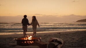 Una pareja caminando por la playa, con un brasero al frente.