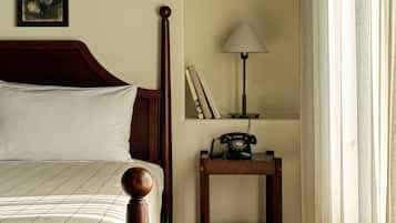 A neatly made bed with a wooden headboard, a bedside lamp, a small table with a telephone, and books on the wall.