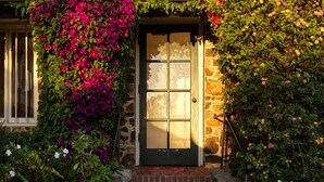 A stone building with a dark door, surrounded by lush greenery and vibrant flowers.