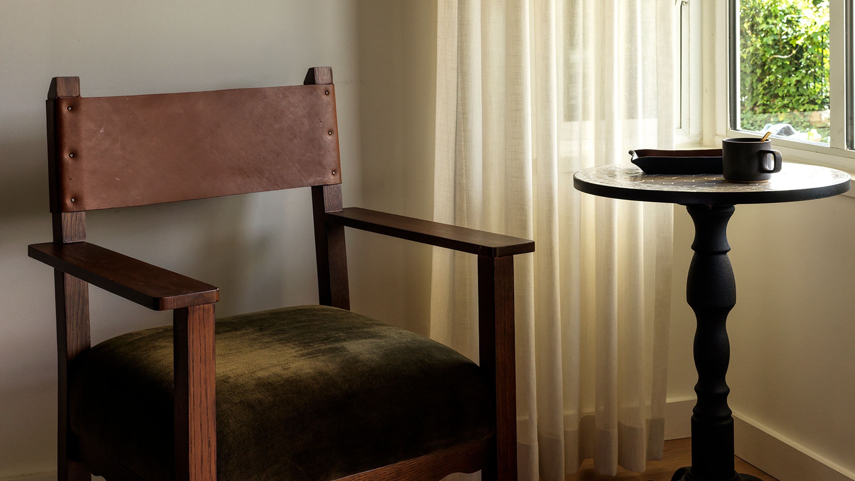 A chair with a wooden backrest and seat, positioned next to a round table with a dark-colored top.