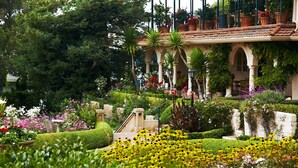 A garden with a variety of flowers and plants, a building with arches and a balcony with potted plants. - La Playa Hotel (Carmel)