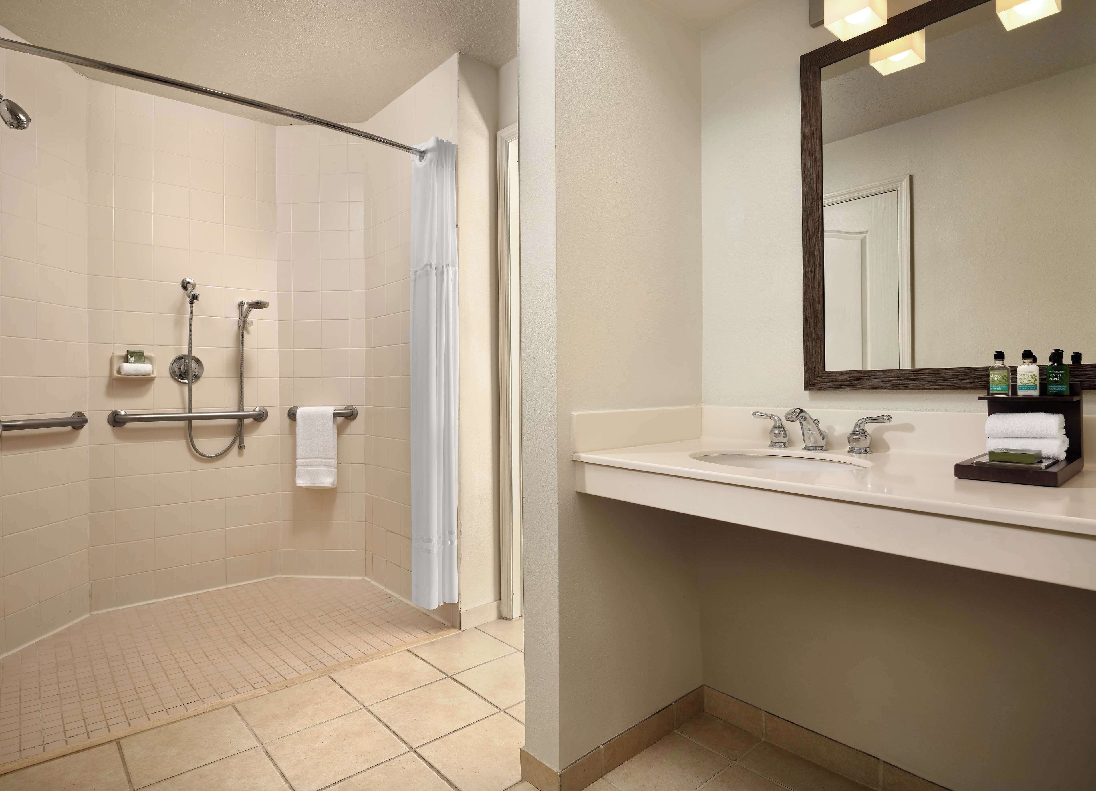 A bathroom with a shower, a sink, a mirror, and toiletries.