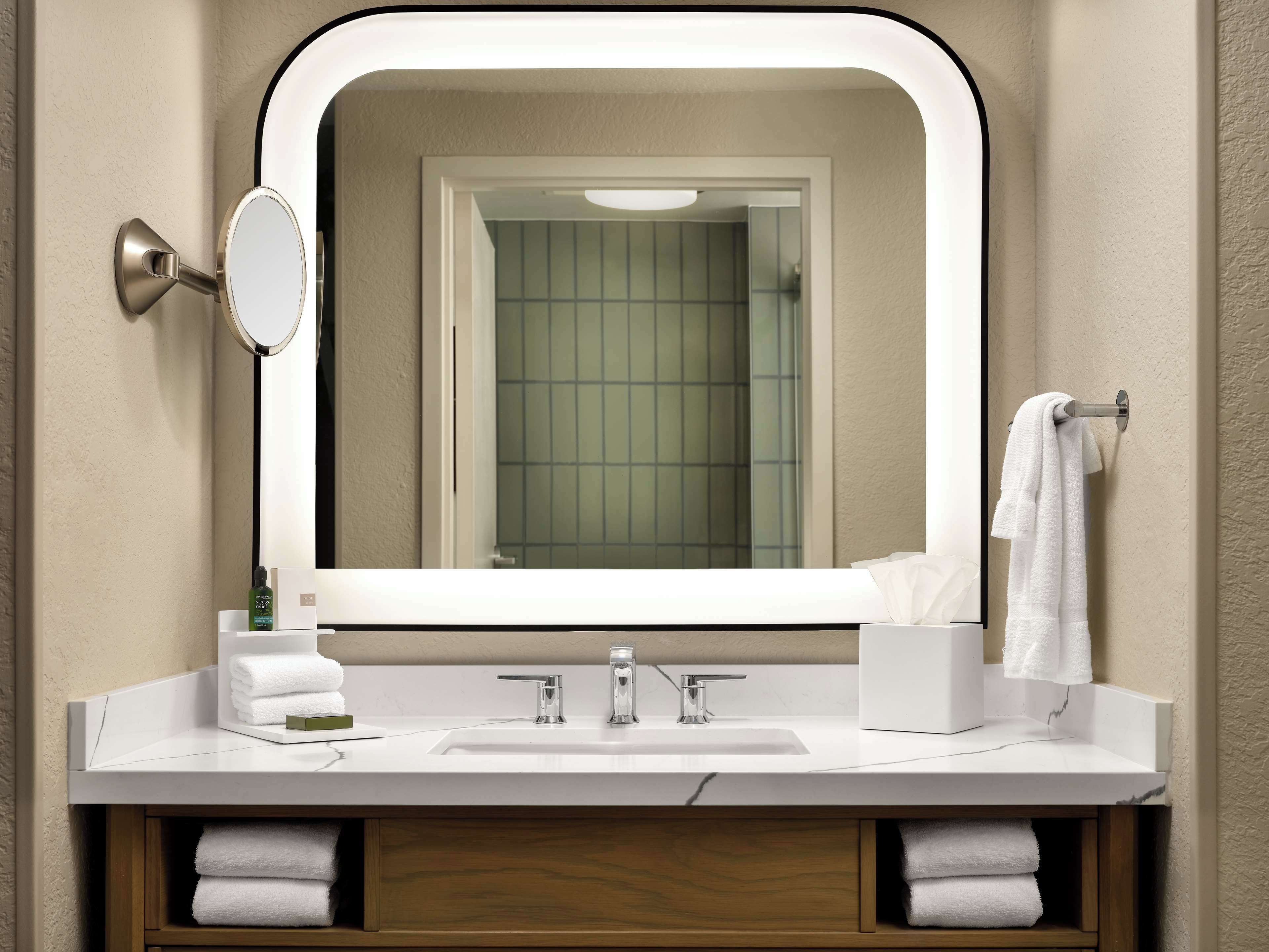 A bathroom with a large mirror, a sink, and a towel rack.