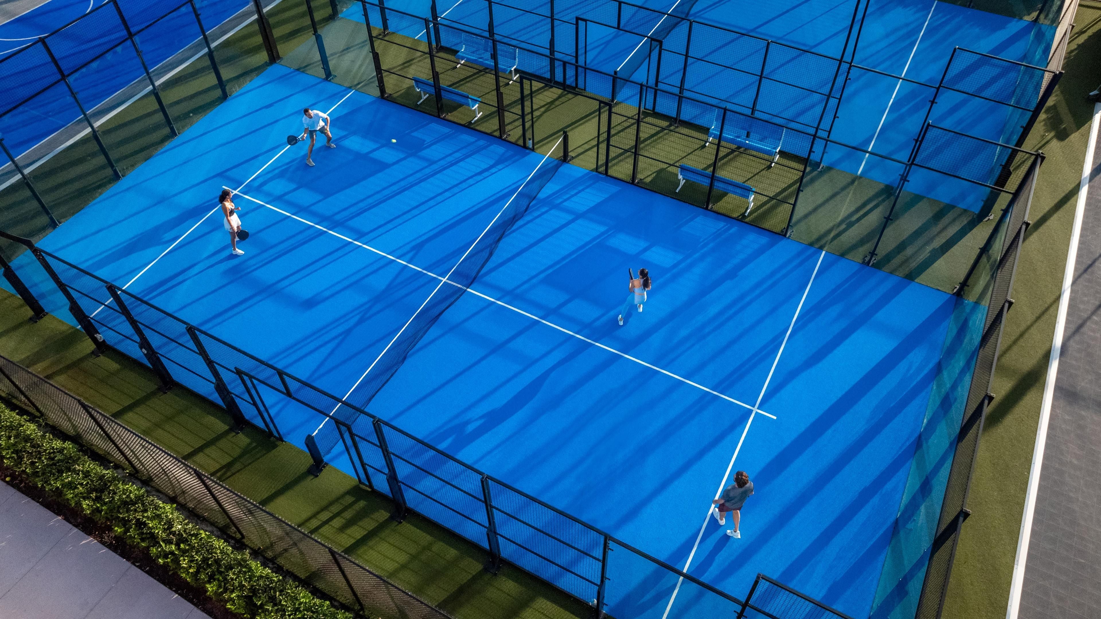 A tennis court with multiple players, surrounded by blue fencing.