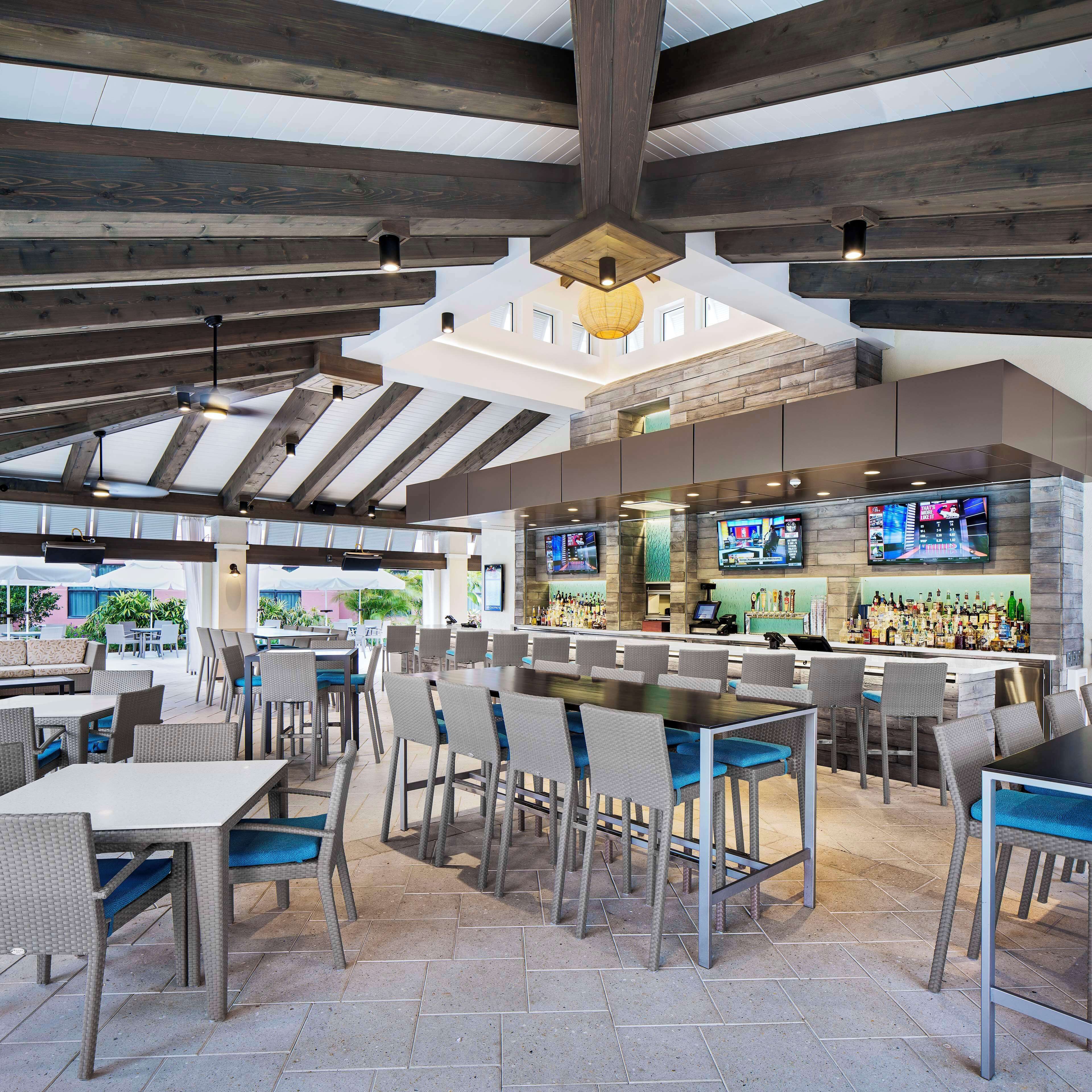 A spacious outdoor dining area with high ceilings and exposed beams, a bar with a variety of liquor bottles, and outdoor seating.