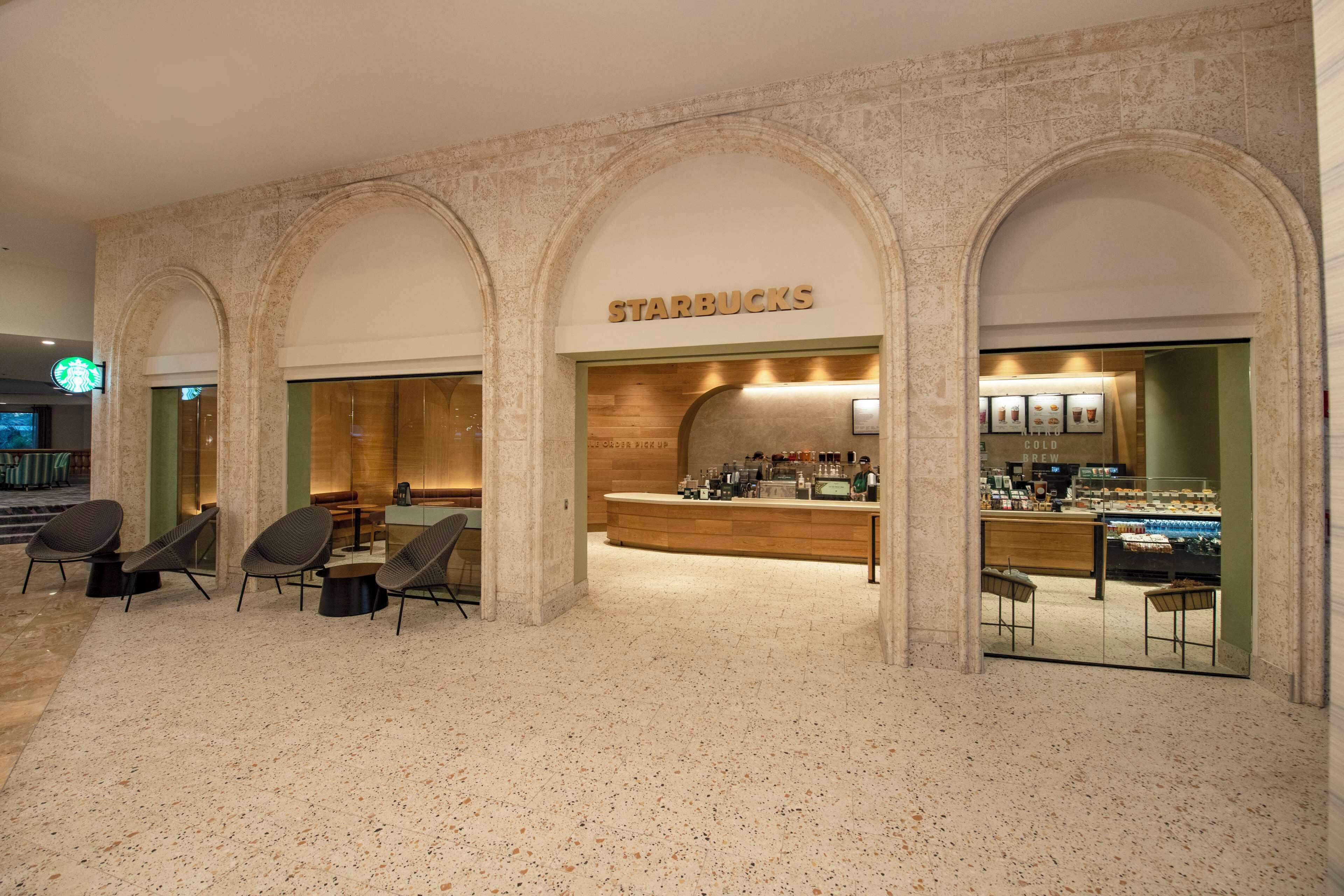 Un Starbucks con mostrador y zona de estar, situado en un edificio con arcos.