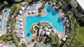 Una vista aerea di un resort con una grande piscina, lettini prendisole e palme.