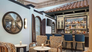 A bar area with a variety of seating options, including patterned chairs and stools, a bar counter with bottles, and a large mirror on the wall.