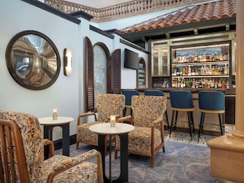 A modern living room with a flat-screen TV, a small refrigerator, a bench, a wicker table, and a colorful rug. at Caribe Royale Orlando, WorldHotels Elite