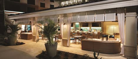 A hotel with an outdoor seating area, a bar, and a pool.