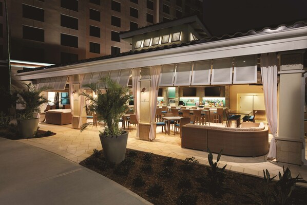 A hotel with an outdoor seating area, a bar, and a pool.