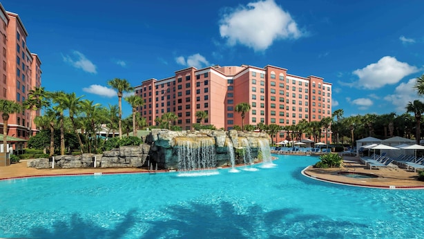 A hotel with a large pool, palm trees, and a waterfall feature.