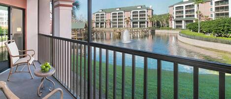 A balcony with a chair, a small table with apples, and a view of a building across a body of water.