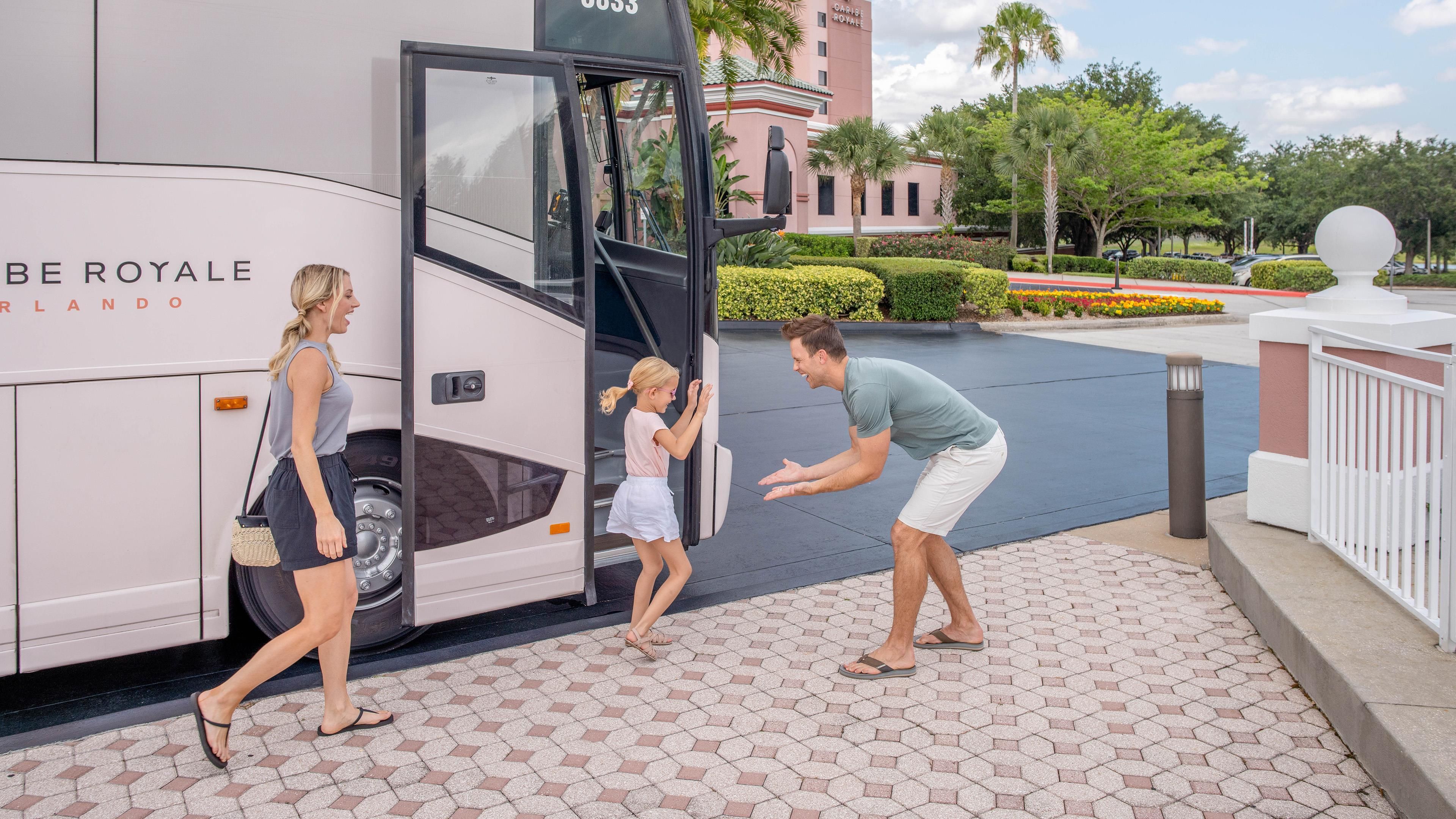 Um ônibus grande com a inscrição 'CARIBE ROYALE', estacionado em área externa bem cuidada, com calçada pavimentada e paisagismo.