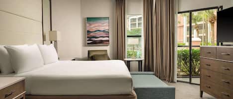 Habitación de hotel con cama, escritorio, silla, cómoda, televisor, un cuadro y ventana con cortinas.