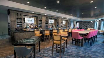 Un área de bar con armarios de madera, una barra y diferentes disposiciones de asientos, incluyendo una mesa redonda y sillas.