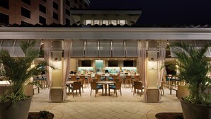 An outdoor dining area with tables and chairs, a bar, and potted plants.