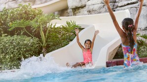 A water slide at a pool with a rocky background and greenery.