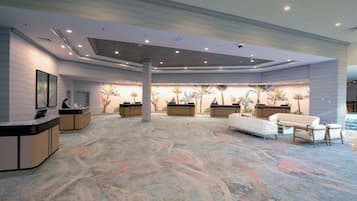 Un vestíbulo espacioso con alfombra estampada, mostradores de recepción y una zona de estar con sofás y sillones.
