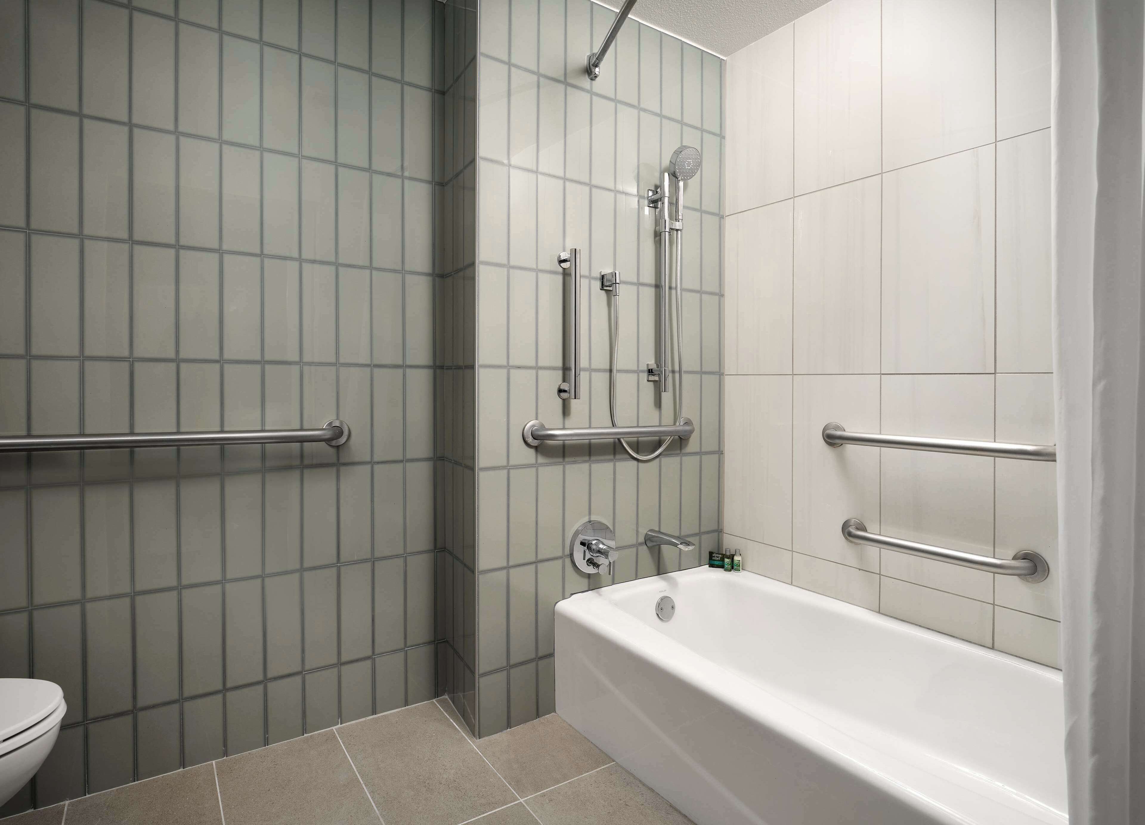 A bathroom with a bathtub, a shower with grab bars, and a toilet.
