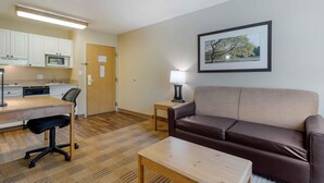 Een knus woongedeelte met een kitchenette, een bank, een bijzettafeltje en een lijst met een foto aan de muur.