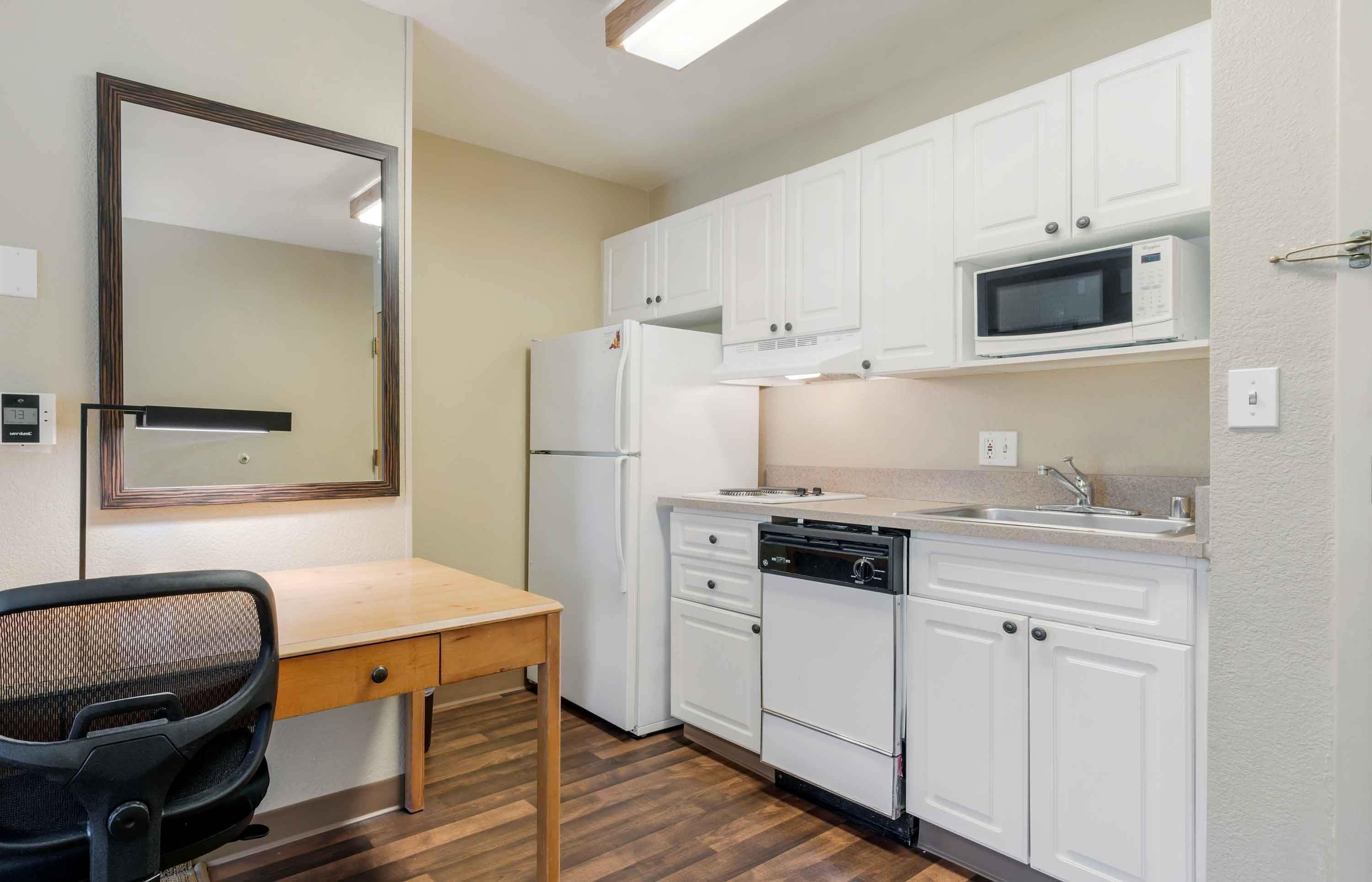 A compact kitchen with white cabinets, a microwave, a refrigerator, and a dishwasher.