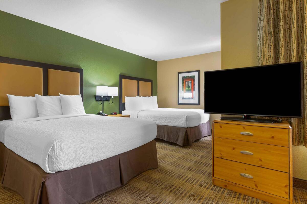 Une chambre d’hôtel avec deux lits, une télévision, une commode et un tableau encadré au mur.